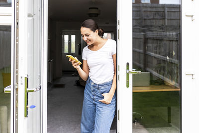 Smiling woman using smart phone in doorway at home