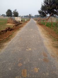 Dirt road amidst field against sky