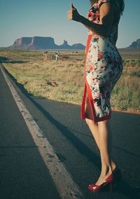 Midsection of woman standing on road against clear sky