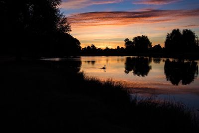 Reflection of silhouette trees in calm lake at sunset