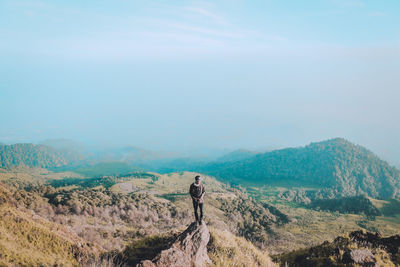 High angle view of young man standing on mountain against sky during sunny day