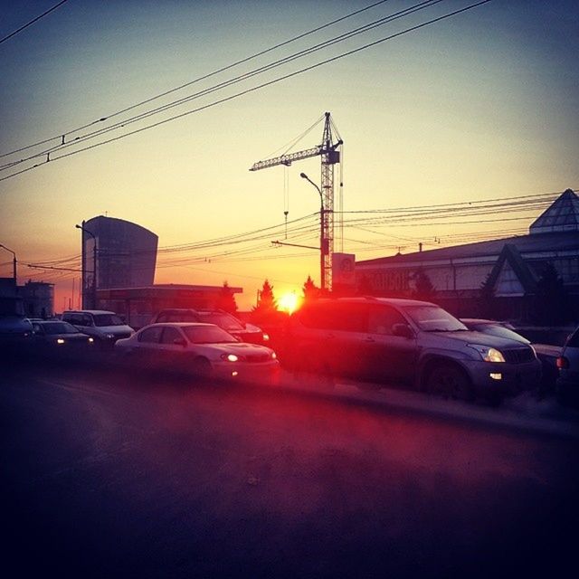 sunset, transportation, car, land vehicle, electricity pylon, mode of transport, building exterior, power line, street, built structure, architecture, road, city, sky, street light, orange color, sun, clear sky, silhouette, electricity