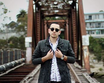 Portrait of young man wearing sunglasses standing on bridge