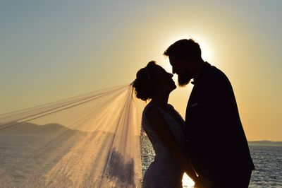Side view of couple kissing against sky during sunset