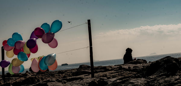 Multi colored balloons on rocks by sea against sky