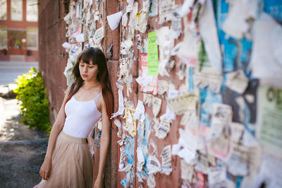 Young woman standing by wall with torn posters