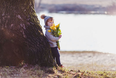 Portrait of boy holding bouquet standing by tree trunk