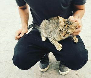 Midsection of man carrying cat while crouching outdoors