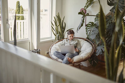 Woman sitting in papasan chair and using laptop