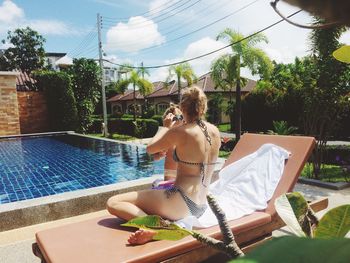 Full length of woman sitting on deck chair by daughter at poolside