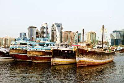 Boats moored on river by buildings against clear sky