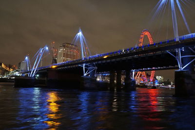 Illuminated bridge over river against sky in city at night