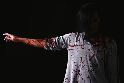 Portrait of man with arm outstretched in zombie costume standing against black background