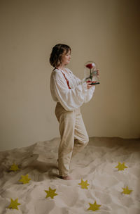 Young female in victorian shirt standing with rose on the sand and smile