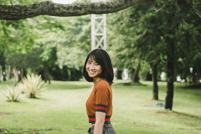 Portrait of smiling young woman standing against trees