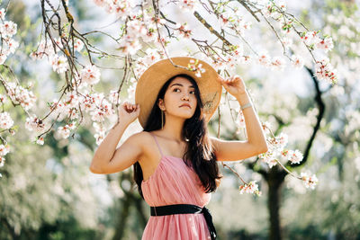 Portrait of beautiful young woman standing by flowering plants