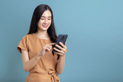 Young woman using mobile phone against blue background