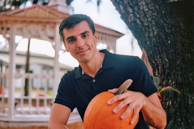 Portrait of young man smiling while holding pumpkin outdoors