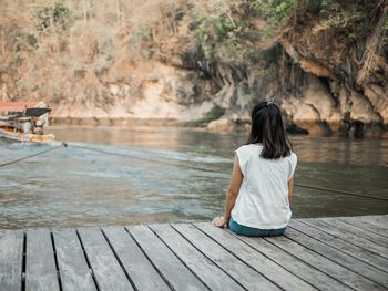 Rear view of woman sitting on wood by lake