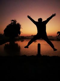 Silhouette man with arms outstretched against sky during sunset