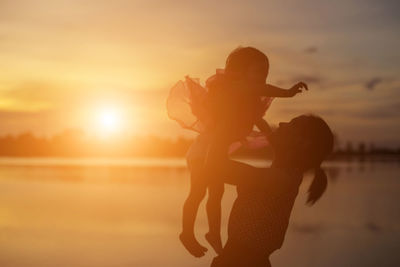 Silhouette woman standing on beach against sky during sunset