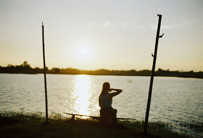 Woman standing at lakeshore against sky during sunset