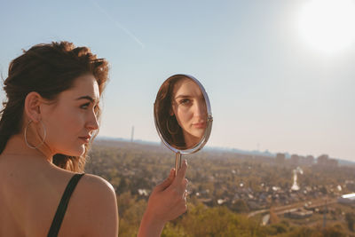 Rear view of young woman looking in mirror against clear sky