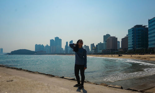 Full length of woman standing by sea in city against clear sky