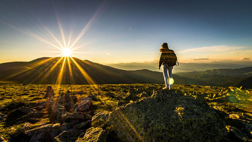 Rear view of woman standing on cliff against sky during sunset