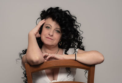 Portrait of smiling woman sitting on chair against gray background