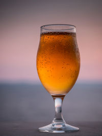 Close-up of beer glass against sea during sunset