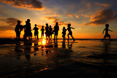 Silhouette people standing at beach during sunset