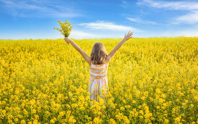 Rear view of woman standing amidst oilseed rape field against sky