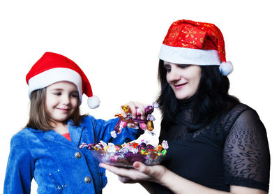 Mother and daughter in santa hats having chocolates against white background