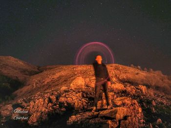 Rear view of man standing on rock at night