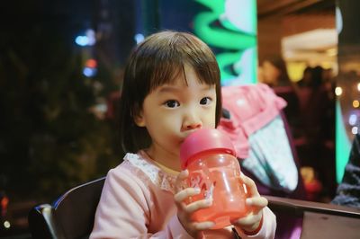 Close-up portrait of cute girl drinking on chair at night