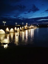 Illuminated bridge over river against sky at night