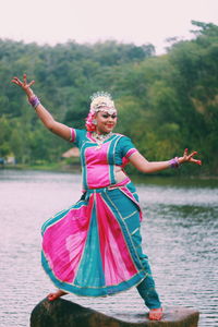 Smiling woman dancing on rock with lake in background