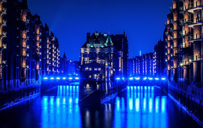 Illuminated buildings by river against sky at night