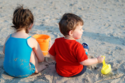 Siblings in bathing suits playing with beach toys in the sand