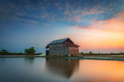 Built structure by lake against sky during sunset