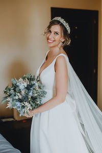 Portrait of smiling bride holding bouquet at home