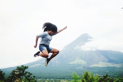 Full length of a woman jumping against mountains