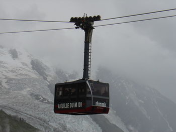 Telephone pole on snow covered mountains against sky