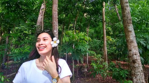 Portrait of smiling young woman standing against trees in forest