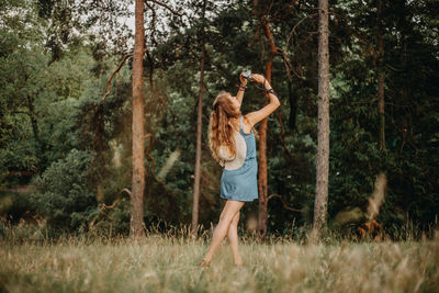 Rear view of woman photographing while standing in forest