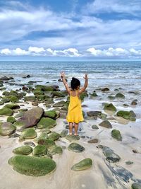 Rear view of girl standing at beach on rock against sky