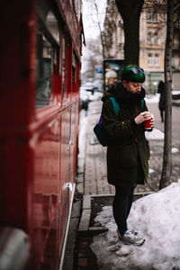 Portrait of non-binary hipster woman standing by red bus in city