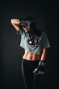 Woman wearing boxing gloves while standing against black background