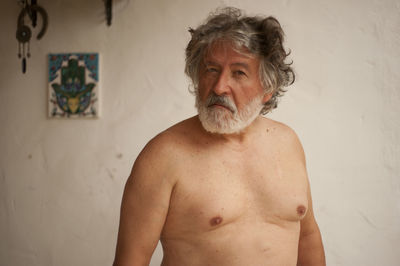 Portrait of shirtless man standing against wall at home